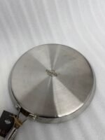 A professional-grade laser-etched non-stick stainless steel crepe pan with a textured honeycomb surface and ergonomic silver handle, shown on a kitchen counter and an induction cooktop.