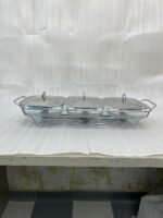 A Paramount Series 3-in-1 buffet food warmer featuring three square glass serving dishes with stainless steel lids on a chrome wire rack, displayed on a kitchen counter and an outdoor dining table with tea light candles lit underneath.