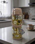 A 1.9-liter olive green Day Days vacuum insulated coffee airpot with a brown pump-action lid and handle, featuring a decorative coffee bean pattern, displayed on a kitchen counter next to a coffee cup.