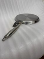 A professional-grade laser-etched non-stick stainless steel crepe pan with a textured honeycomb surface and ergonomic silver handle, shown on a kitchen counter and an induction cooktop.