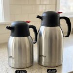 Stainless Steel Thermal Flask with a black lid and handle, available in 1.5 liter and 2 liter sizes, shown on a kitchen countertop.