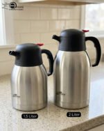 Stainless Steel Thermal Flask with a black lid and handle, available in 1.5 liter and 2 liter sizes, shown on a kitchen countertop.
