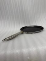 A professional-grade laser-etched non-stick stainless steel crepe pan with a textured honeycomb surface and ergonomic silver handle, shown on a kitchen counter and an induction cooktop.