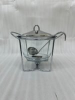 A 4-liter Paramount Series food warmer featuring a clear glass bowl, stainless steel stand, and lid, shown on a dining table with guests and filled with warm lentil soup.