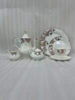 Elegant super bone china tea set featuring a teapot, teacup, plates, cream pitcher, and sugar bowl with a brown vintage baroque pattern and gold rims, displayed on a wooden table.