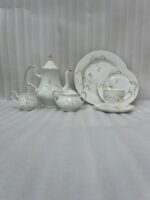 A luxury floral super bone china tea set, including a teapot, creamer, sugar bowl, plates, and a steaming cup of tea, arranged on a wooden outdoor table during sunset.