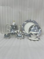 A premium grey and white floral pattern super bone china tea set featuring a teapot with gold accents, a creamer, a sugar bowl, plates, and a filled teacup with a saucer on a wooden table.