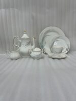 Luxury super bone china tea set featuring a teapot, teacup, saucer, creamer, and sugar bowl with fine gold trim and soft grey feather patterns on a wooden table.