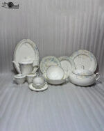 A comprehensive 61-piece super bone china dinner set for an 8-person serving, displayed on a wooden table against a neutral background. The white ceramic tableware features a delicate light blue and grey floral pattern with thin silver rims. The set includes a large oval platter, dinner plates, side plates, soup bowls, a covered casserole dish, a teapot, a creamer, a sugar bowl, and tea cups with saucers.