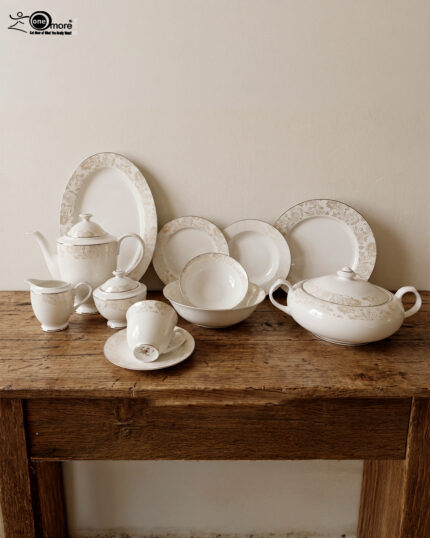 A comprehensive 61-piece super bone china dinner set arranged for display against a neutral textured background. The white porcelain tableware features a delicate cream and gold floral pattern on the rims. The collection includes dinner plates, side plates, soup bowls, a large oval platter, a lidded serving tureen, a teapot with matching sugar bowl and creamer, and teacups with saucers