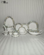 A photograph of a One More Super Bone China 61-piece dinner set arranged on a dark walnut wood table against a neutral beige wall. The luxurious set, designed for 8-person serving, features white bodies and elegant grey-gold marble-pattern rims with subtle gold detailing. It displays a variety of plates, a matching teapot, a large covered tureen, open serving bowls, a cream pitcher, and teacups with saucers. The brand logo is visible in the top left corner