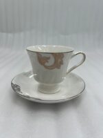 A luxury white super bone china cup and saucer featuring gold leaf designs and a gold rim, set on a white placemat on a wooden dining table.
