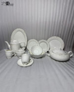 A comprehensive collection of 61 pieces of white bone china dinnerware featuring an intricate gold and cream floral pattern with gold rims, arranged elegantly on a wooden table.