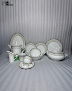 An elegant 61-piece white super bone china dinner set arranged on a polished wooden table against a neutral beige wall. The porcelain tableware features sophisticated silver-grey textured borders and includes dinner plates, bowls, a large oval serving platter, a covered soup tureen, and a complete tea service with a teapot, creamer, sugar bowl, cups, and saucers