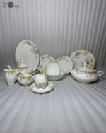 An elegant 61-piece One More brand super bone china dinnerware set with gold rims and soft floral patterns, arranged beautifully on a wooden table with a white runner