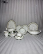 An elegant 61-piece super bone china dinnerware set for an 8-person serving, featuring white plates, bowls, a teapot, a covered tureen, and teacups with detailed beige and silver patterned rims, neatly arranged on a wooden table