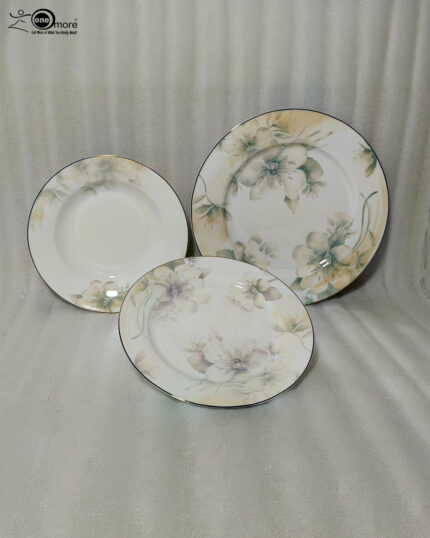 A beautifully stacked 18-piece premium Super Bone China plate set featuring an elegant floral pattern and fine trim, arranged on a beige linen table runner alongside crystal wine glasses and a rustic flower vase.