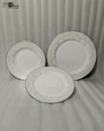 A stacked 18-piece OneMore super bone china dinnerware plate set featuring elegant cream plates with intricate lace damask borders, displayed on a dark wooden table with a silver runner and stainless steel cutlery