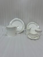 A complete 24-piece luxury tea set on a wooden table, featuring a white porcelain teapot, milk jug, sugar pot, cups, saucers, and plates with delicate silver fern patterns.