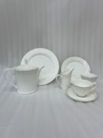A complete 24-piece white porcelain tea set featuring delicate lace-patterned edges and silver trim, arranged on a wooden table.