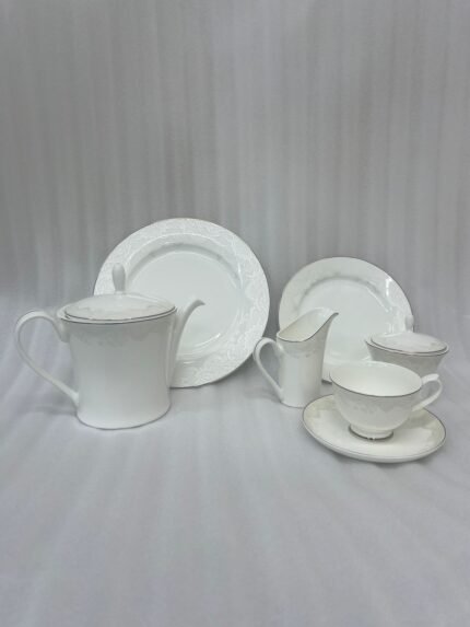 A complete 24-piece white porcelain tea set featuring delicate lace-patterned edges and silver trim, arranged on a wooden table.