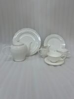A 24-piece white porcelain tea set featuring a delicate silver floral scroll pattern, including a teapot, cups, saucers, plates, and serving pots, arranged on a wooden table.