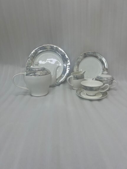 A 24-piece porcelain tea set featuring a modern grey marble pattern border with silver accents, including a teapot, milk pot, sugar bowl, cups, saucers, and plates arranged on a wooden surface.