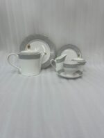 A 24-piece luxury porcelain tea set featuring a crisp white finish, sophisticated grey floral patterned rims, and delicate gold accents, arranged on a glossy surface.