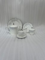 A sophisticated 24-piece white porcelain tea set featuring a delicate grey floral pattern and silver trim, arranged elegantly on a table runner.