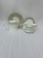 A 24-piece luxury porcelain tea set featuring white ceramic with a soft green brushstroke border and gold-tone accents, arranged on a light wooden table.