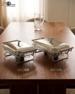 Two Paramount Series stainless steel food warmers in 2L and 3L sizes on a wooden table, featuring glass basins and polished metal lids.