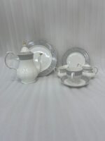 : A complete 24-piece white porcelain tea set featuring delicate grey floral patterns with gold trim, including a teapot, teacups, saucers, and plates, arranged on a wooden surface.