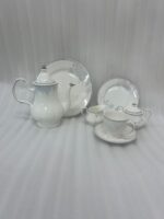 A 24-piece white porcelain tea set featuring delicate gray floral patterns and silver trim, arranged on a light wooden surface.