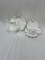 A luxurious 24-piece white porcelain tea set featuring delicate gold filigree patterns, including a teapot, teacups, saucers, plates, and serving pieces displayed on a marble-textured surface