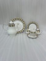 : A complete 24-piece porcelain tea and dining set featuring white ceramic with gold and olive-green striped rims, including plates, cups, saucers, a teapot, a sugar bowl, and a milk creamer arranged on a wooden surface.