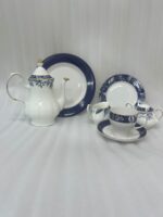 A 24-piece luxury porcelain tea set featuring a classic blue and white floral pattern with gold trim, including a teapot, cups, saucers, and plates, arranged on a beige table runner.
