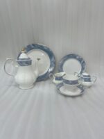 A 24-piece luxury porcelain tea set featuring a white base with elegant blue marble-patterned rims and gold accents, displayed on a textured stone surface including a teapot, cups, saucers, plates, sugar pot, and creamer.