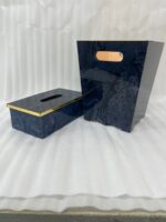 A luxury blue marble resin tissue box cover and matching wastebasket with elegant gold trim on dark wooden tables in a bathroom setting.