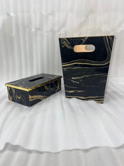 Luxury black and gold marble pattern dustbin and matching tissue box holder on a wooden vanity next to a marble bathroom sink.