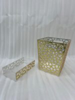 Clear acrylic tissue box holder and matching small desktop dustbin with an elegant gold geometric lattice pattern on a wooden desk.