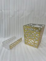 Clear acrylic dustbin and matching tissue box holder with a gold geometric lattice pattern on a white marble tabletop.