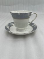 Elegant white Super Bone China tea cup and saucer with a grey floral pattern and gold rim, filled with tea and garnished with star anise and a jasmine flower on a wooden table