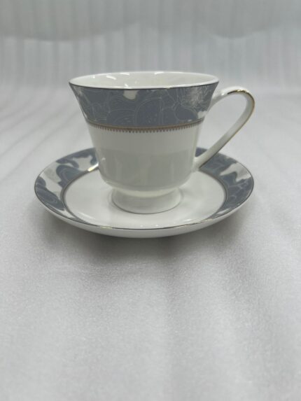 Elegant white Super Bone China tea cup and saucer with a grey floral pattern and gold rim, filled with tea and garnished with star anise and a jasmine flower on a wooden table