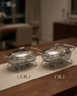 Two Paramount Series stainless steel oval food warmers in 2.4L and 3L sizes on a table runner, featuring glass bowls and polished metal lids.