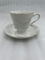 Steaming hot tea in an elegant white bone china teacup with gold trim and a silver leaf design, resting on a matching saucer on a wooden table