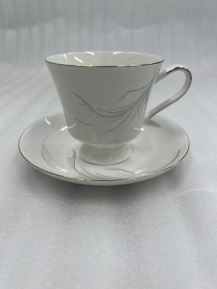 Steaming hot tea in an elegant white bone china teacup with gold trim and a silver leaf design, resting on a matching saucer on a wooden table