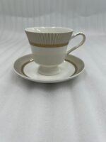 A premium white Super Bone China tea cup and saucer set featuring gold vertical stripes and a gold laurel wreath pattern on a dark wooden table