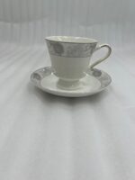 Elegant white Super Bone China teacup and saucer featuring a grey floral pattern and gold rim, placed on a wooden table next to a silver spoon and lavender vase
