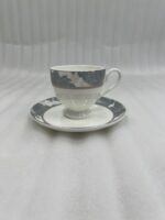 A high-angle shot of a premium super bone china cup and saucer filled with milk tea, featuring a grey floral pattern and silver spoon, set on a wooden table in a cozy living room with green sofas and a fireplace.