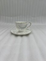 A luxury white super bone china teacup filled with creamy tea, featuring gold-rimmed edges and a delicate grey leaf pattern, resting on a matching saucer on a dark wooden table in a cozy, blurred library background